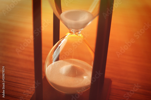 Hourglass with white sand on wooden table, closeup