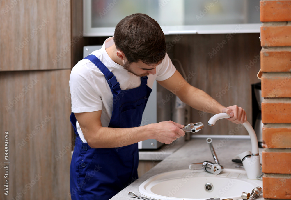 Handsome plumber replacing faucet in kitchen Handsome plumber replacing faucet in kitchen