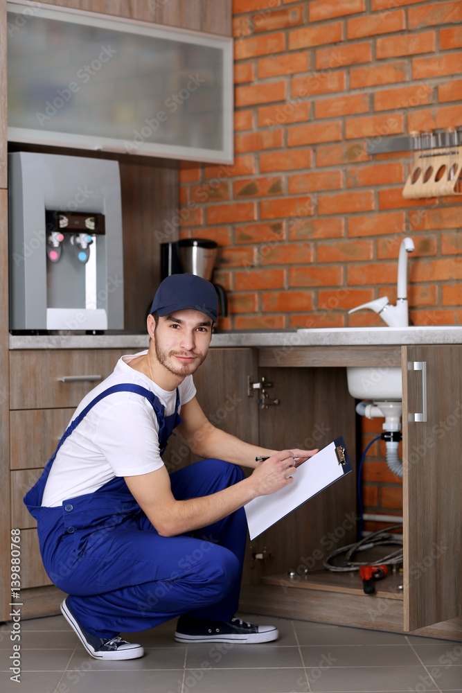 Handsome plumber with pen and clipboard in kitchen