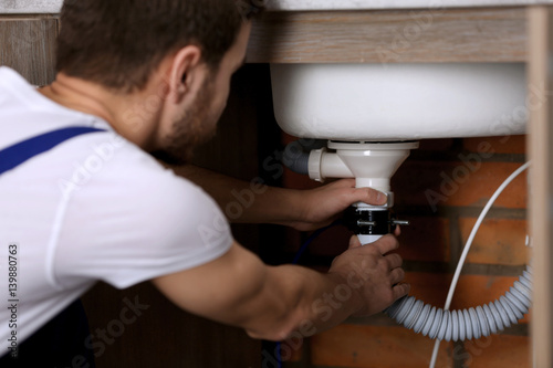 Foto Handsome young plumber repairing sink pipes in kitchen