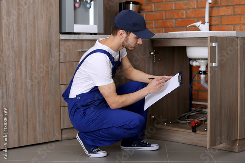 Handsome plumber with pen and clipboard in kitchen