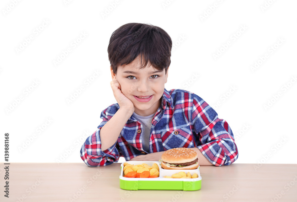 Cute little boy with lunchbox sitting at table, on white background Cute little boy with lunchbox sitting at table, on white background