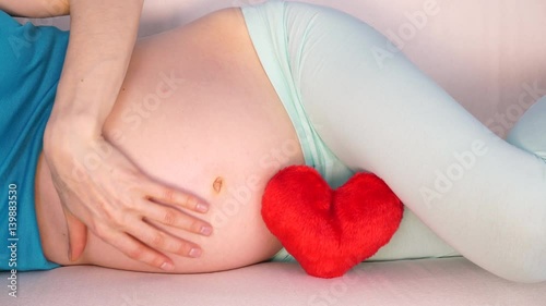 Wallpaper Mural Pregnant woman future mother lying on couch with red heart love symbol, caressing her naked belly. Pregnancy, motherhood and baby anticipation concept. 4K ProRes HQ codec Torontodigital.ca