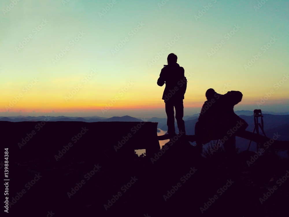 silhouette picture of two men are standing at the cliff in sunset time. Picture with copy space.