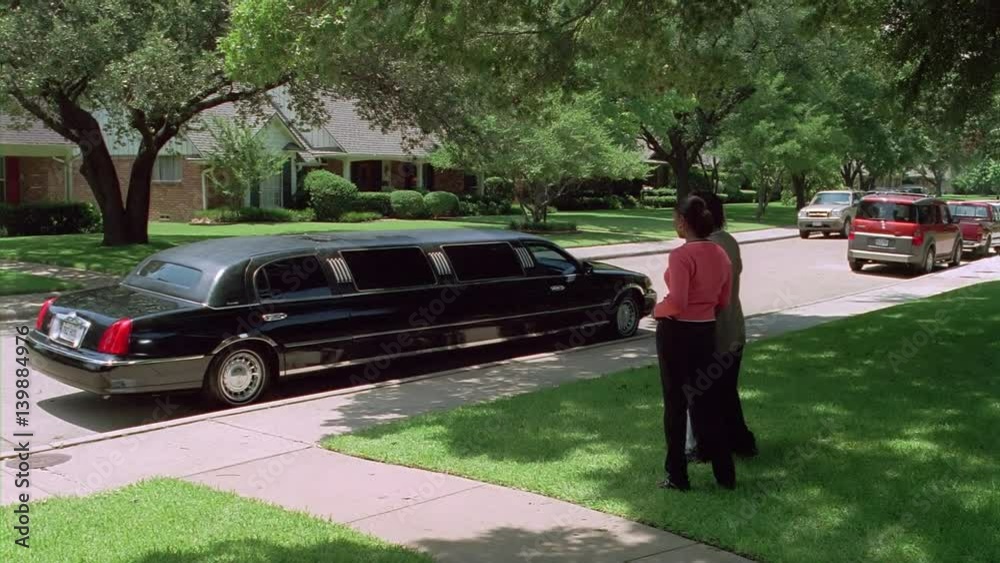 Stretch limo driving away as three people on a lawn wave good-bye and turn away Stretch limo driving away as three people on a lawn wave good-bye and turn away