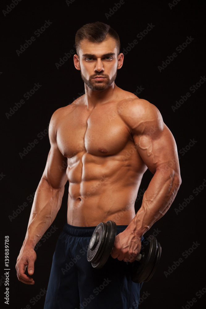 Handsome power athletic man with dumbbell is confidently looking forward. Strong bodybuilder with six pack, perfect abs, shoulders, biceps, triceps and chest Isolated on black background with