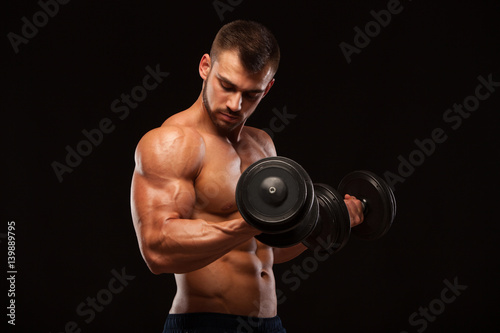 Muscular handsome man is training with dumbbells in gym. isolated on black background with copyspace © satyrenko