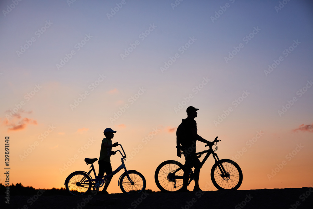 Obraz premium Biker family silhouette, father with kid on bikes at sunset