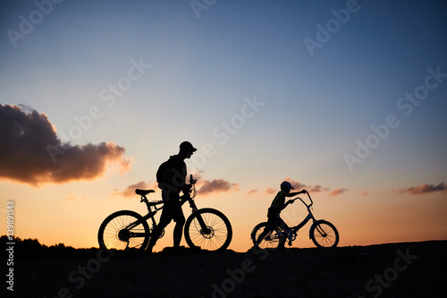 Biker family silhouette, father with kid on bikes at sunset © Shcherbakova