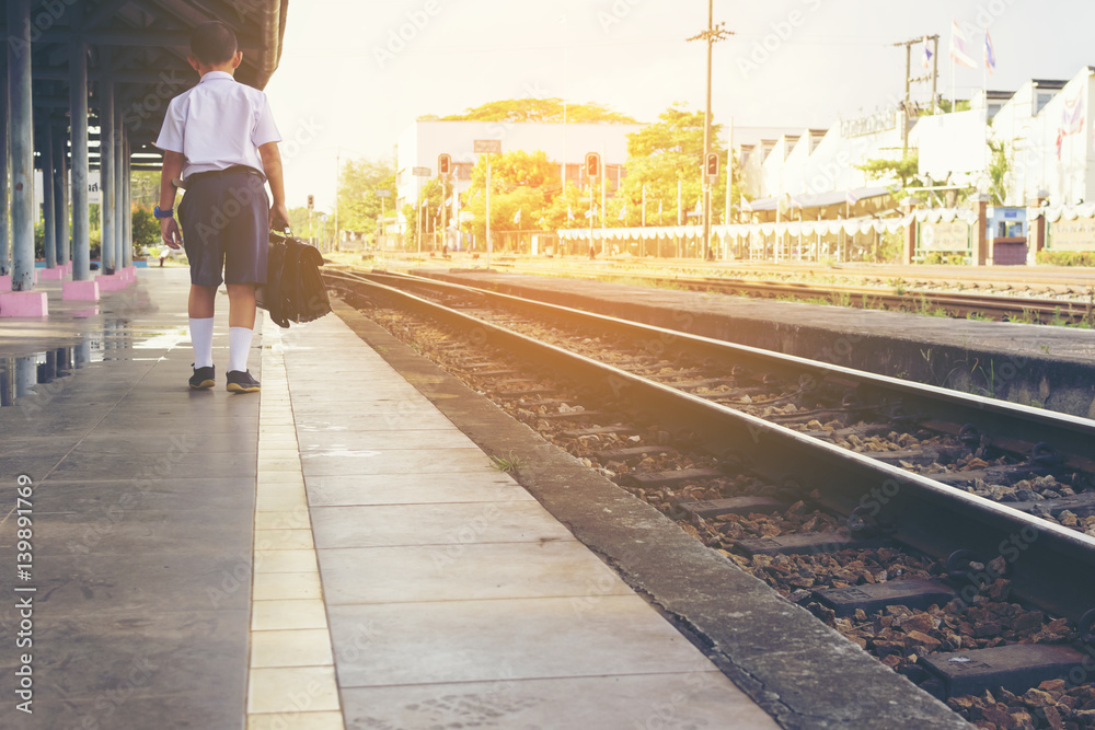 Fototapeta premium Asian boy waiting train at train station.Back of child with sunset.