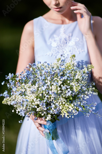 blue bouquet in hands of the girl in a blue dress.  Lilies of the valley and forget-me-nots