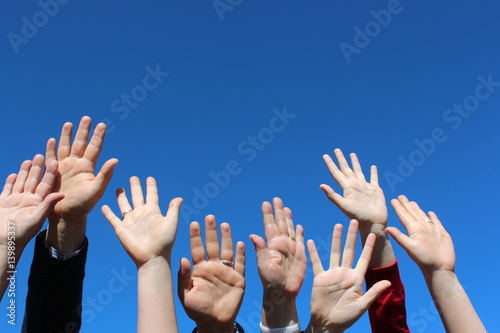 Row of hands with open palms on blue sky background