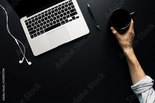 Hand placing mug next to computer on dark, black desk