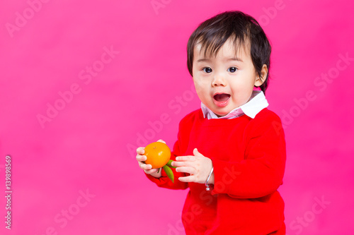 Excited little baby boy holding a Mandarin orange