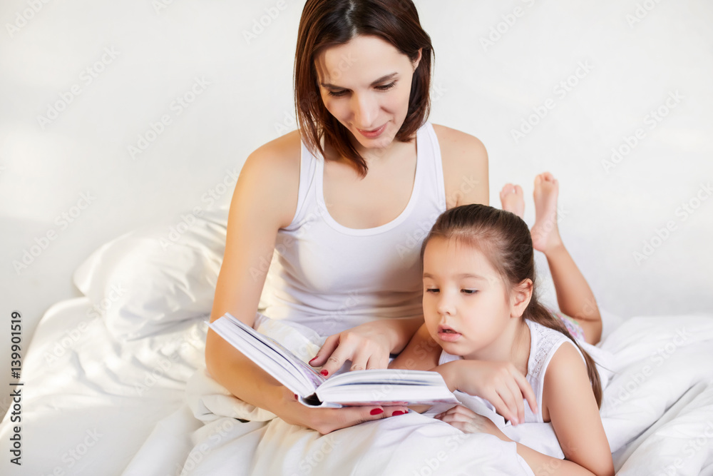 young mother and child reading a book in bed young mother and child reading a book in bed