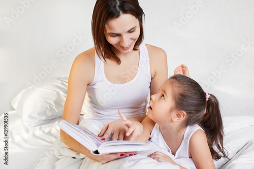 young mother and child reading a book in bed