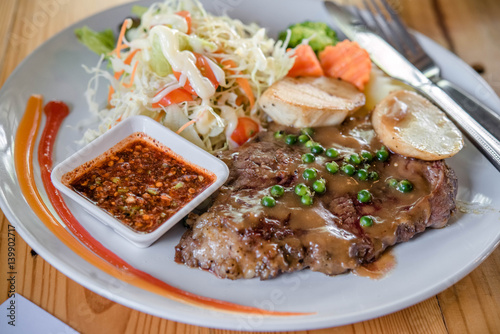 Beef steaks with grilled vegetables and seasoning on wooden background