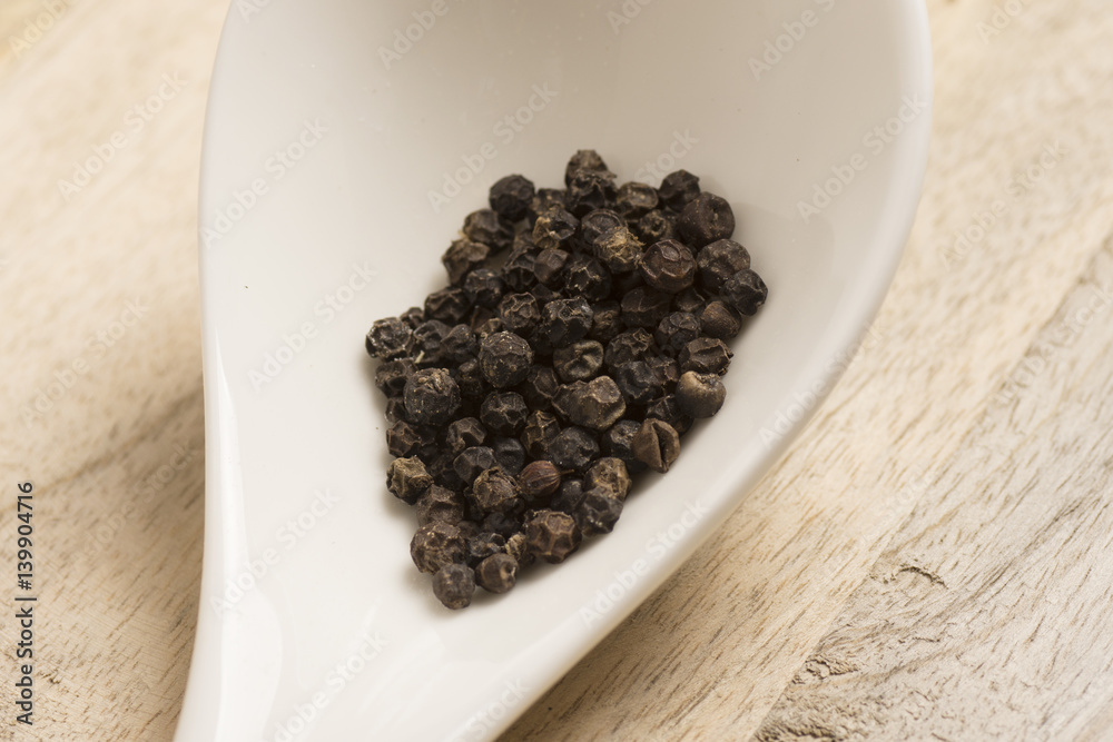 black pepper in white spoon on wooden background black pepper in white spoon on wooden background