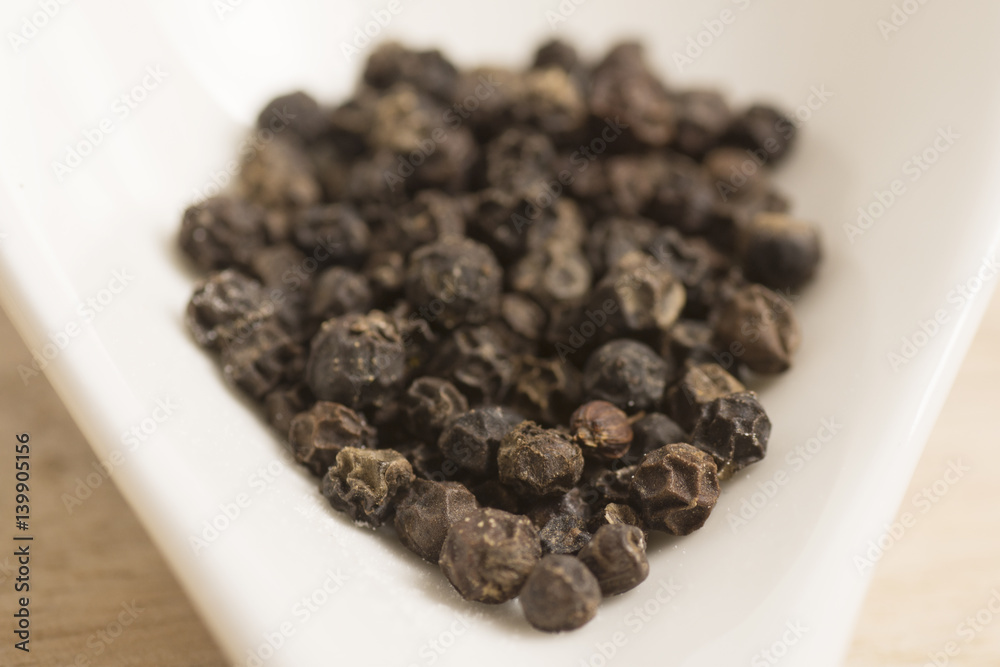 black pepper in white spoon on wooden background black pepper in white spoon on wooden background