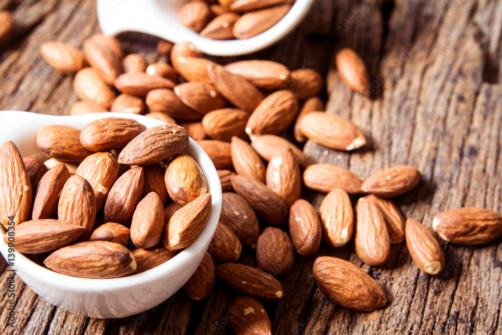close up Peeled almonds nut in small white cup on wooden background close up Peeled almonds nut in small white cup on wooden background