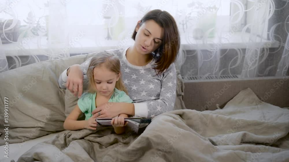 Little girl dressed in a blue T-shirt and striped trousers, shows his mother figure, which she recently painted markers. Mom gently touching blond hair girl, enjoying success in drawing daughter