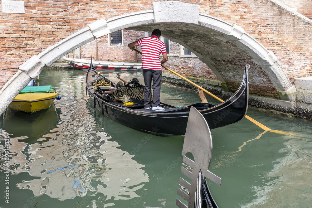 Gondolier passes with some difficulty under a low bridge in the historic center of Venice, Italy