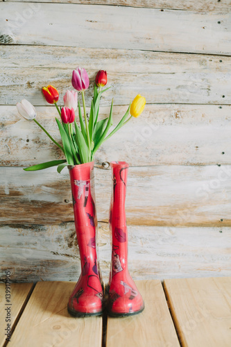colorful rain boots with spring flowers  in wooden background.