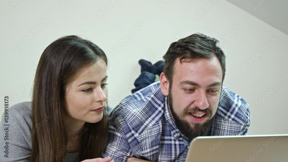 Smiling marriage watching move using a laptop lying on a bed at home Smiling marriage watching move using a laptop lying on a bed at home