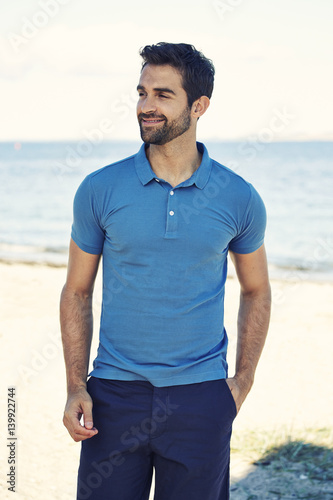 Guy in blue polo shirt on beach, smiling