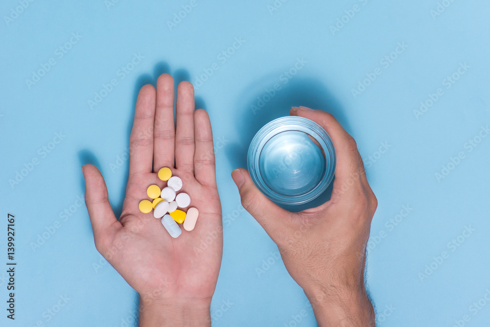 Colored pills in hand with water on blue background.
