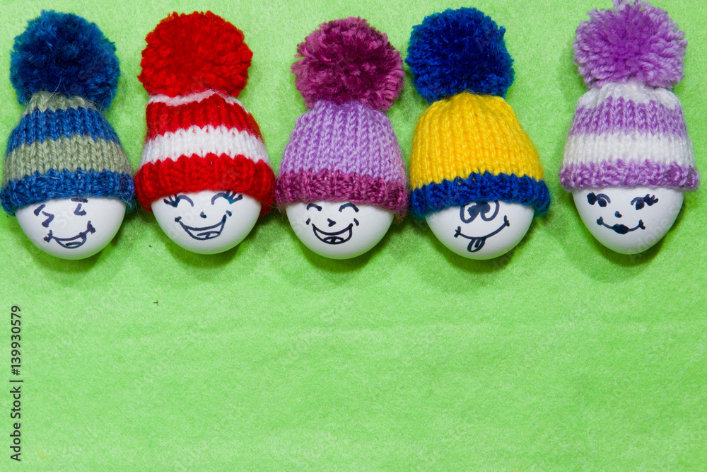 Easter eggs on green felt. Emoticons in knitted hat with pom-poms.