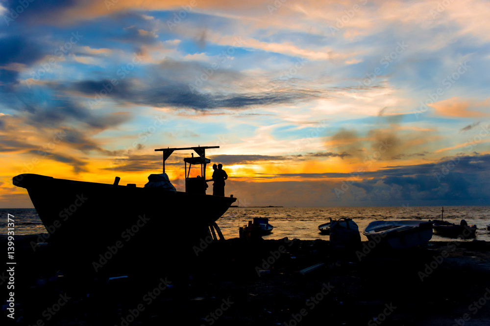 Two fishermen are fixing their boat with Indian ocean sunset background