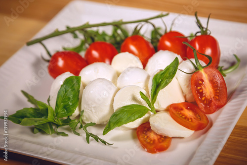 A  gourmet dish - mozzarella with basil, cherry tomatoes and arugula on a white plate