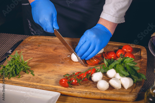 Chef hands with gloves cooked. Chef  is cooking a  gourmet dish - mozzarella with basil, cherry tomatoes and arugula. photo