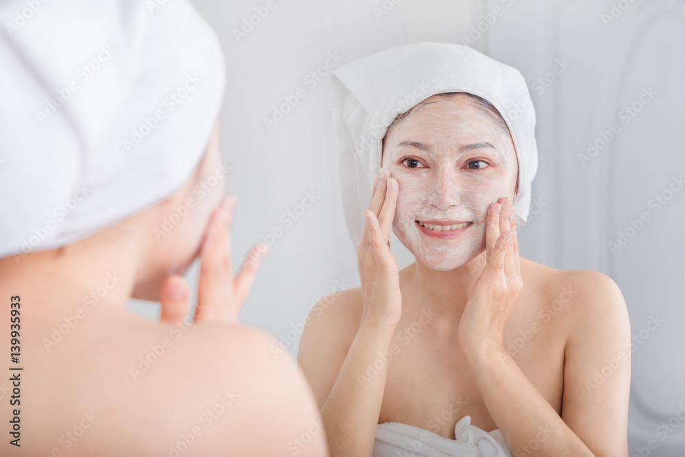 woman applying mask on her face and looking in the mirror woman applying mask on her face and looking in the mirror