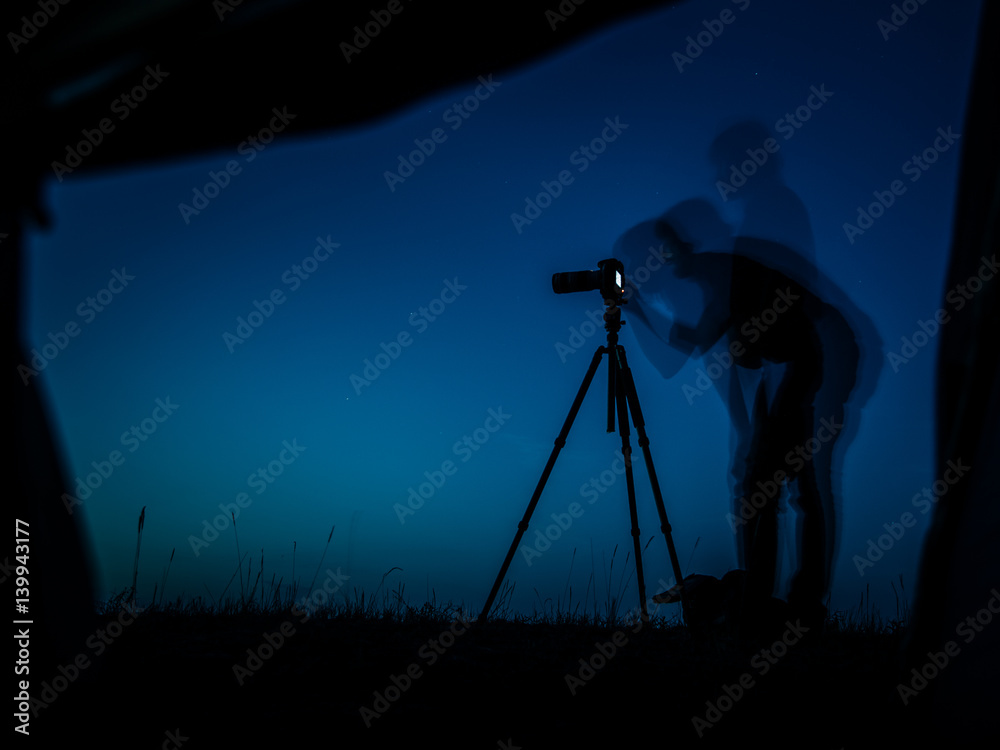 Artistic long exposure photo of a photographer in action. Multiple silhouettes and a camera un tripod.  A view from a tent in night