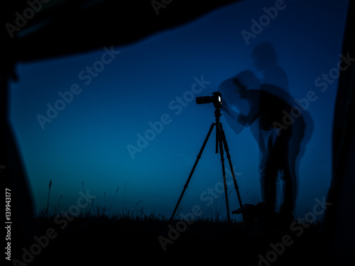 Artistic long exposure photo of a photographer in action. Multiple silhouettes and a camera un tripod. A view from a tent in night