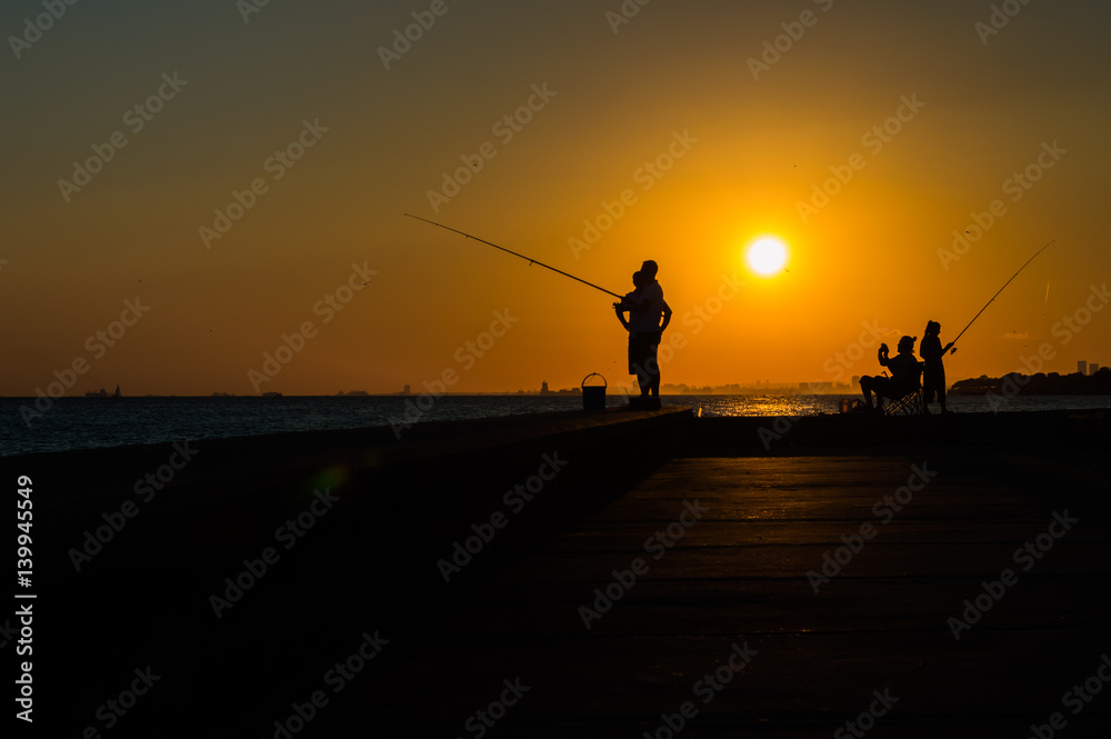 Silhouettes of fishermen by the sea at sunset