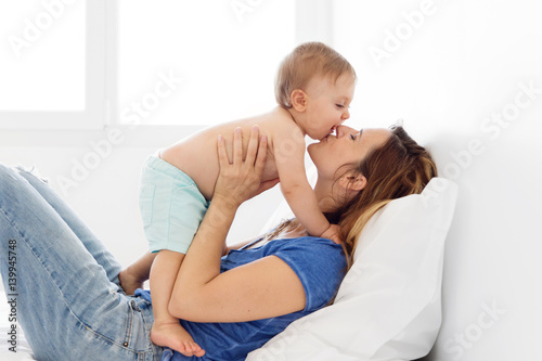 mother lying down on the bed hloding her baby and kissing him photo