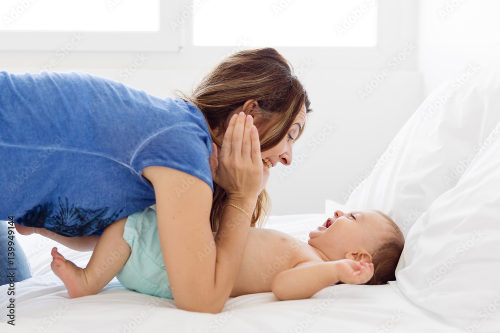 mother and baby playing peek-a-boo and laughing together on the bed mother and baby playing peek-a-boo and laughing together on the bed