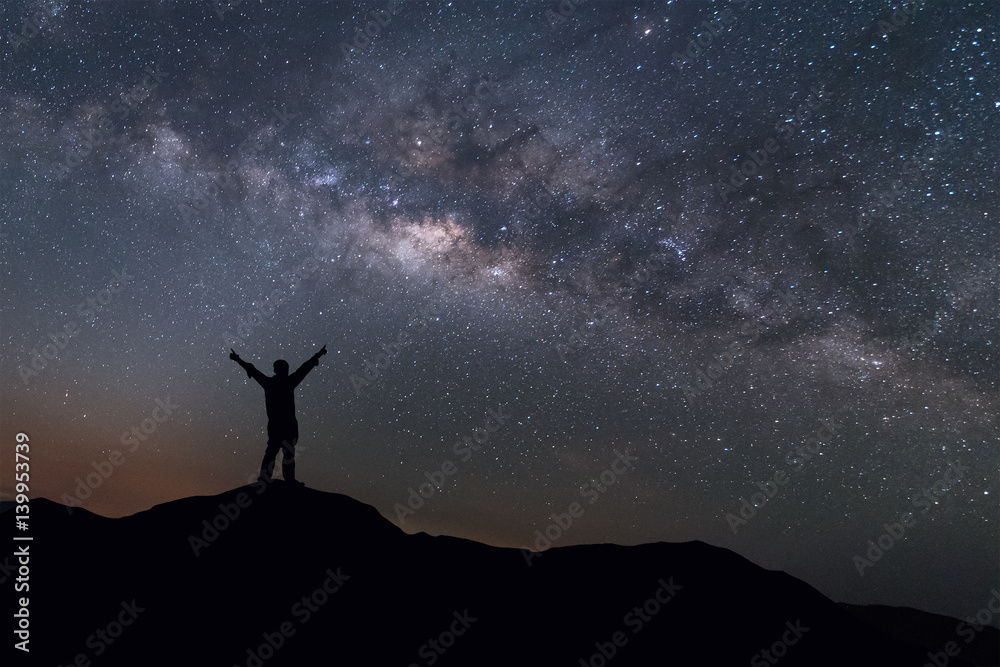Milky Way landscape. Silhouette of Happy man standing on top of mountain with night sky and bright star on background.