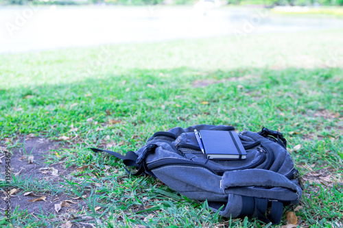Fotografi Notebook and a pen is placed on black backpack in shady tree in the garden with holiday
