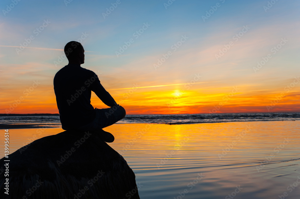 Man silhouette sitting on stone at the seaside contemplating sunset