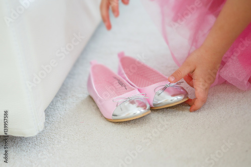 A little girl in a pink dress prepares to reconcile two shoes to the ball