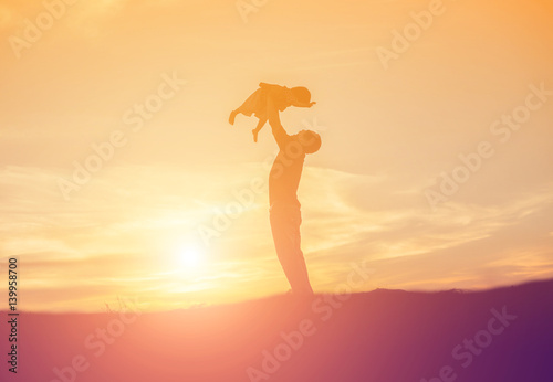 Silhouettes of father and little daughter walking at sunset