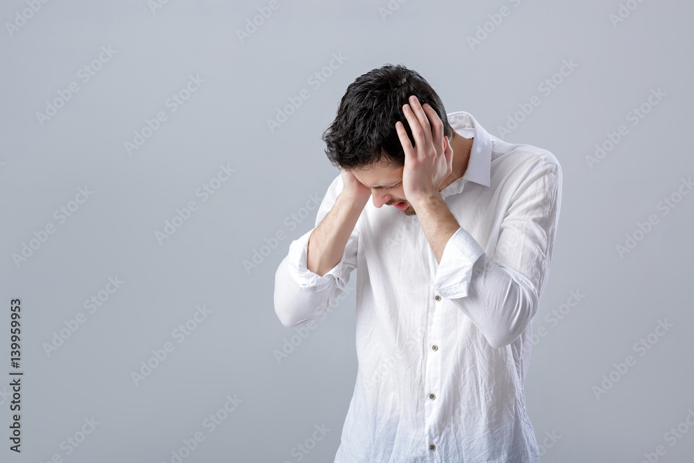 Frustrated young brunette man in shirt with headache on gray bac Frustrated young brunette man in shirt with headache on gray bac