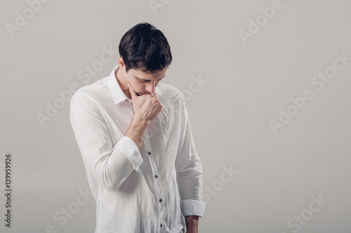 portrait of handsome young pensive man in white shirt on gray ba