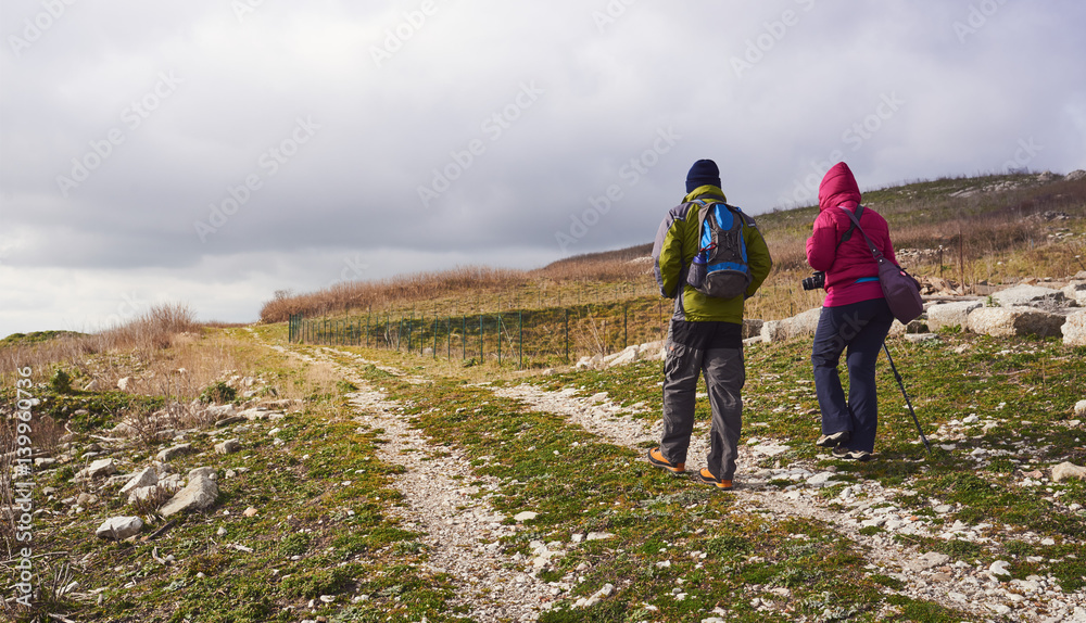 Obraz premium Man and woman hikers trekking in mountains. Young couple walking with backpacks in mountains.