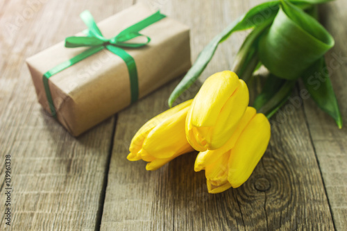 Three yellow tulips and gift box on wooden table