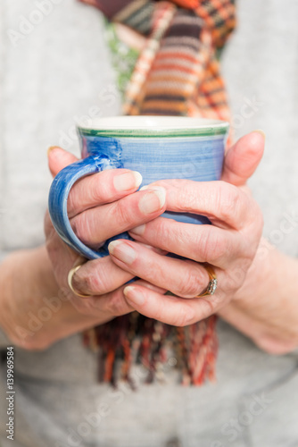 Close up of pensioners hands holding a hot drink.